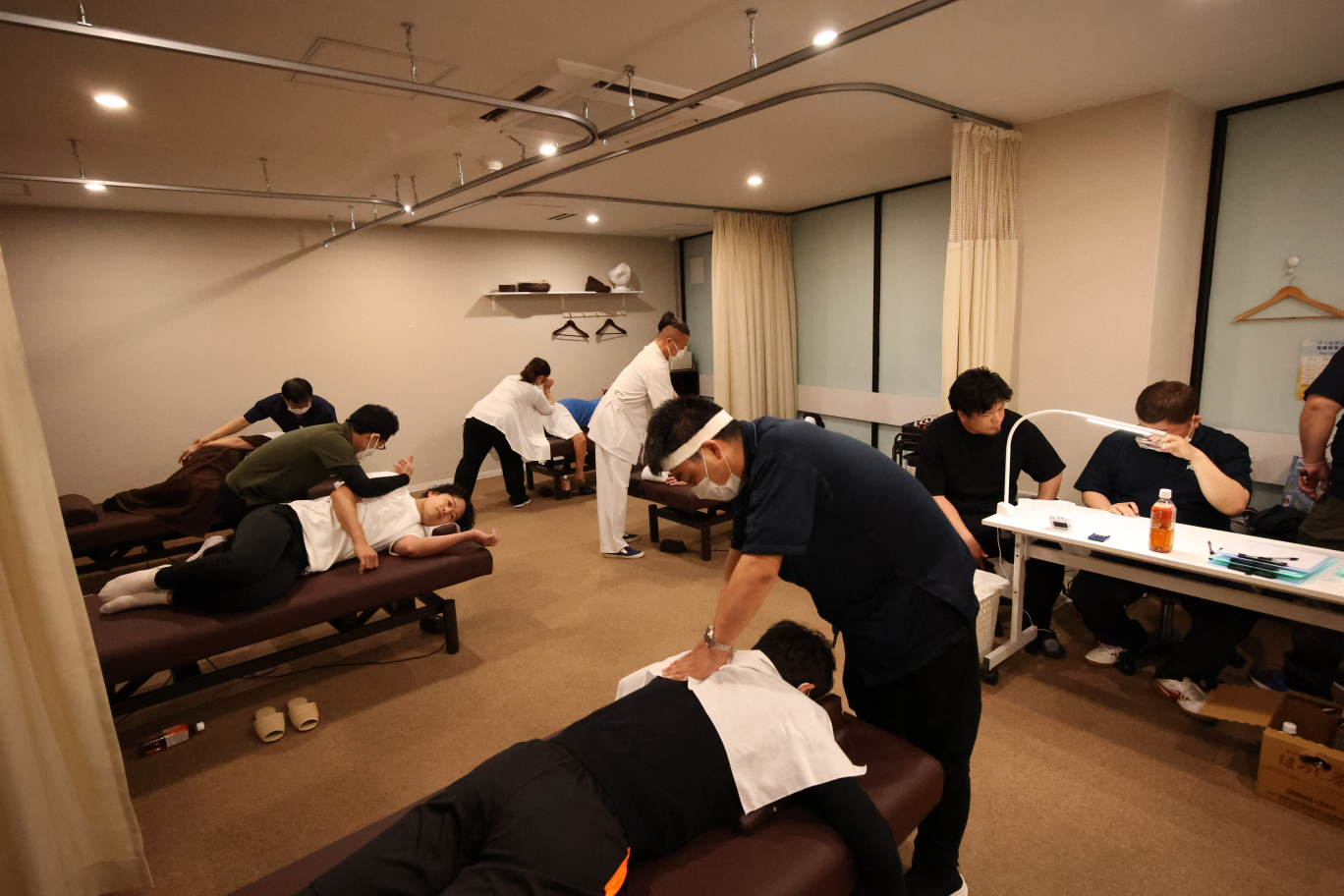 マッサージ施術中の人が複数と審査員がいる会場.