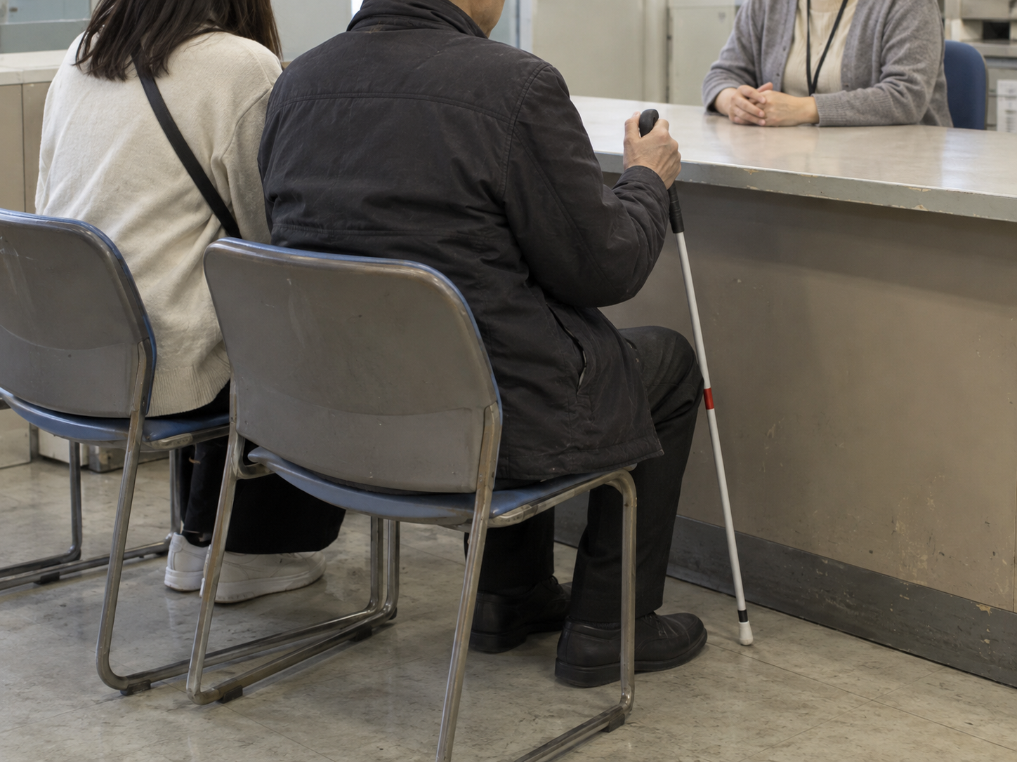 区役所の窓口で、白杖を持つ人と家族が職員に相談する様子